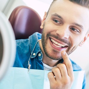 Man smiling at reflection in handheld mirror