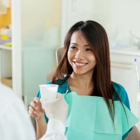 Dentist handing a cup of water to a smiling patient
