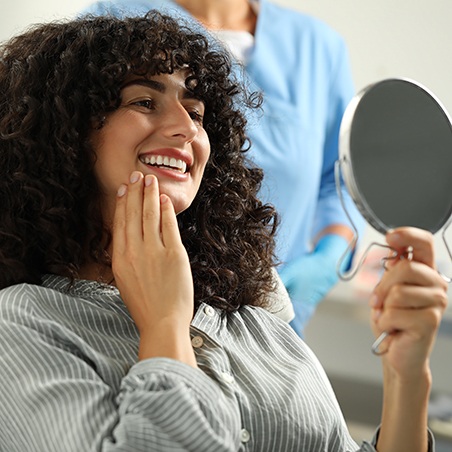 Woman smiling at reflection in handheld mirror