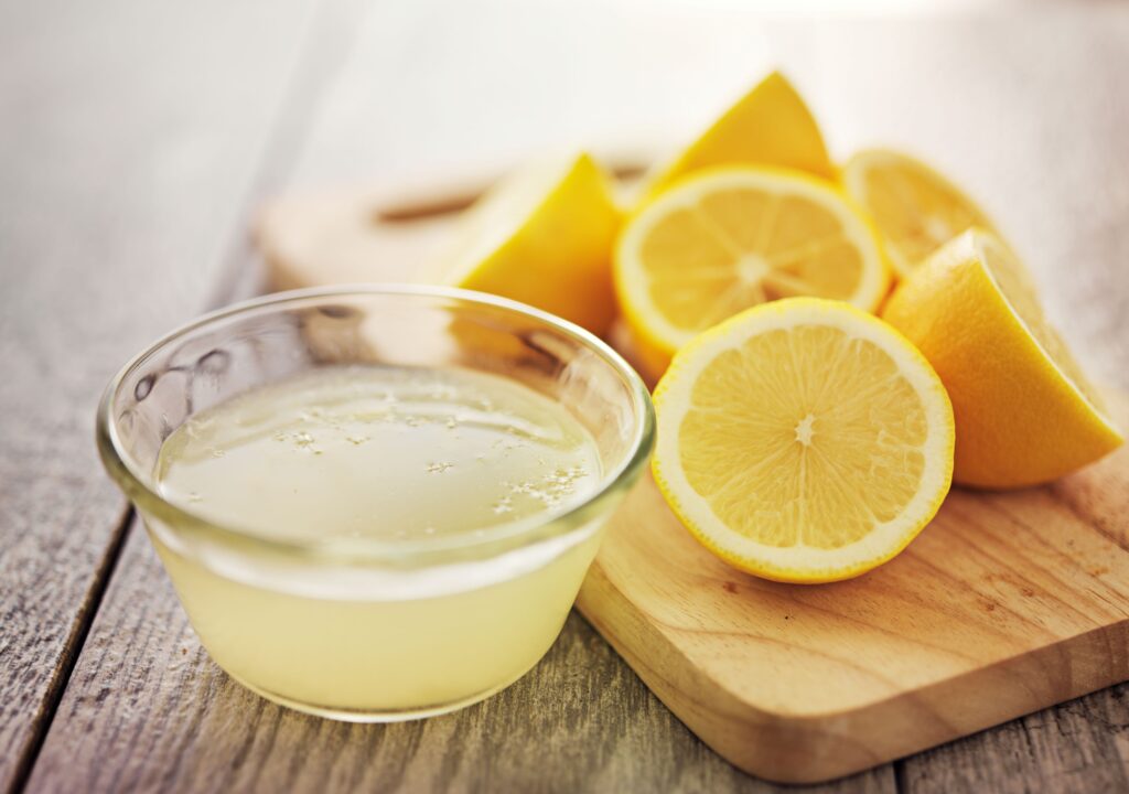 Lemons on cutting board next to small bowl of lemon juice
