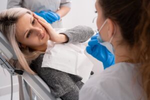 Woman in dentist's chair holding side of face in pain. 