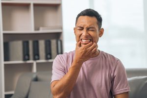 Man squinting in pain holding fingers to corners of his mouth